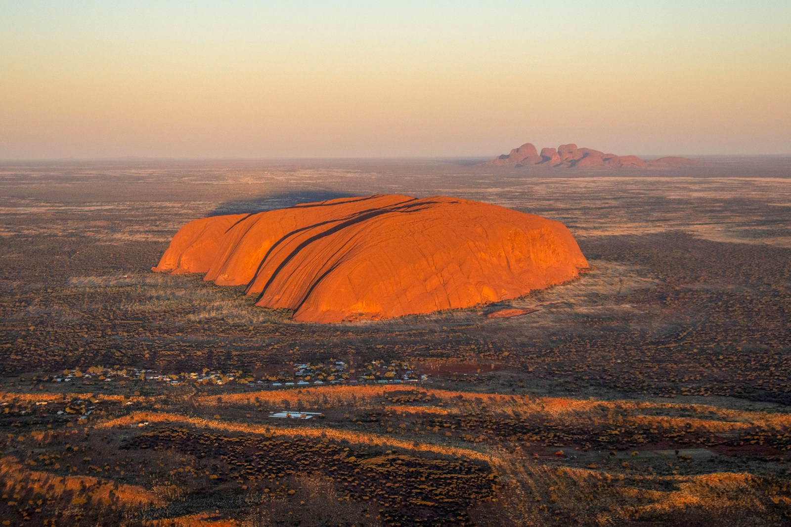 Uluru glowing red at sunset in the Australian outback, with Kata Tjuta on the horizon