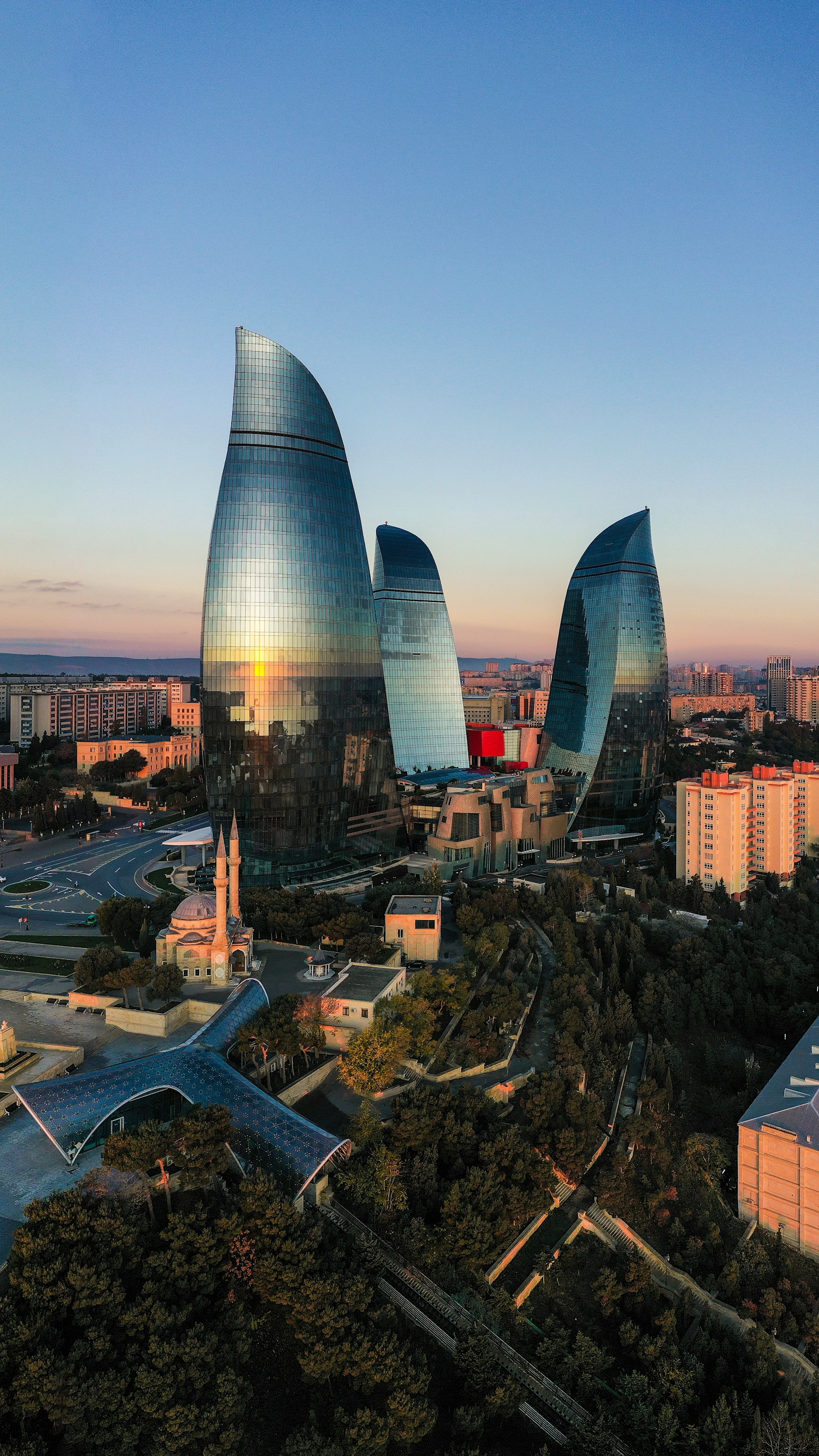 The three glass Flame Towers of Baku glowing at sunset above the city and Caspian