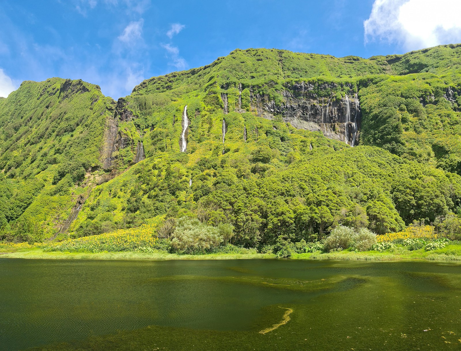 Waterfalls cascading down a green cliff into a lake on Flores, Azores
