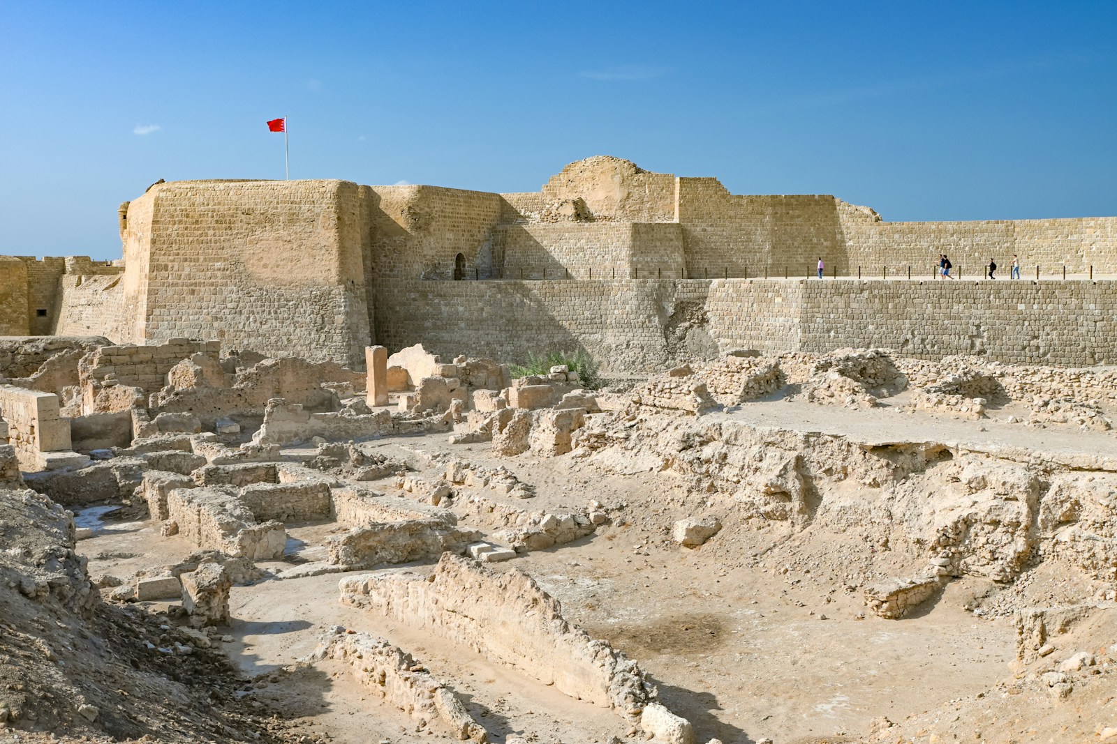 The stone walls of Qal'at al-Bahrain fort above the excavated Dilmun ruins under a clear sky