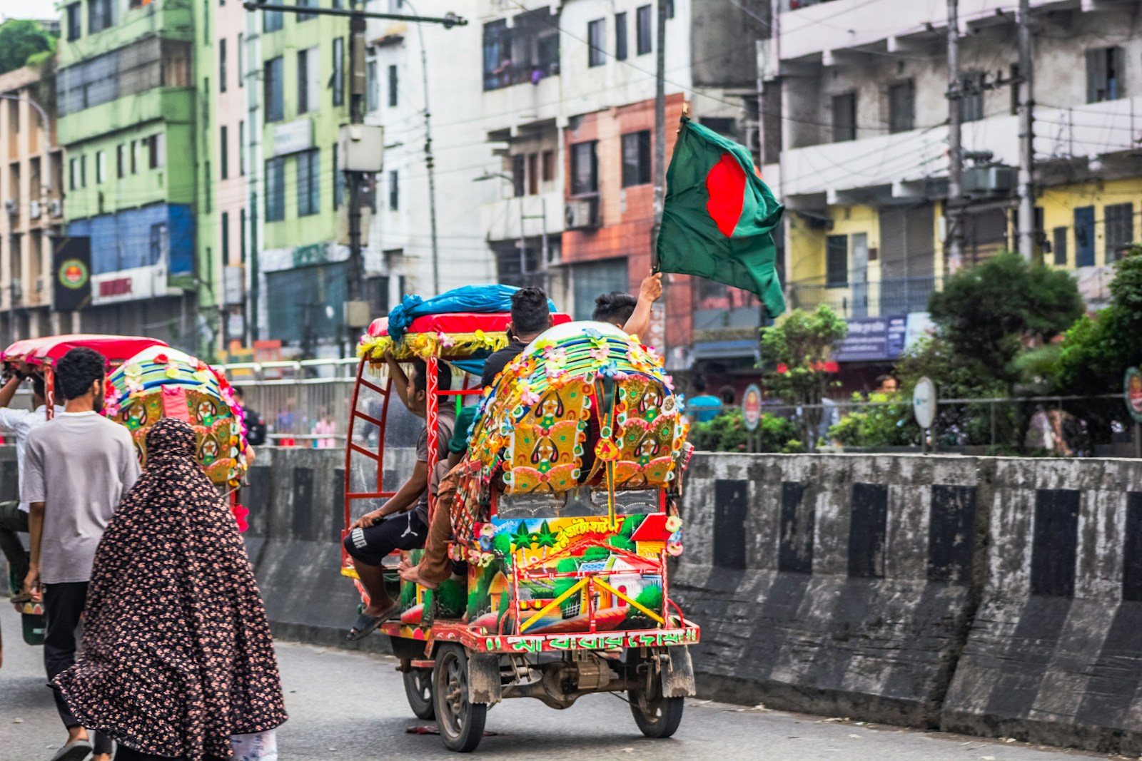 A decorated auto-rickshaw flying the Bangladesh flag on a busy Dhaka street