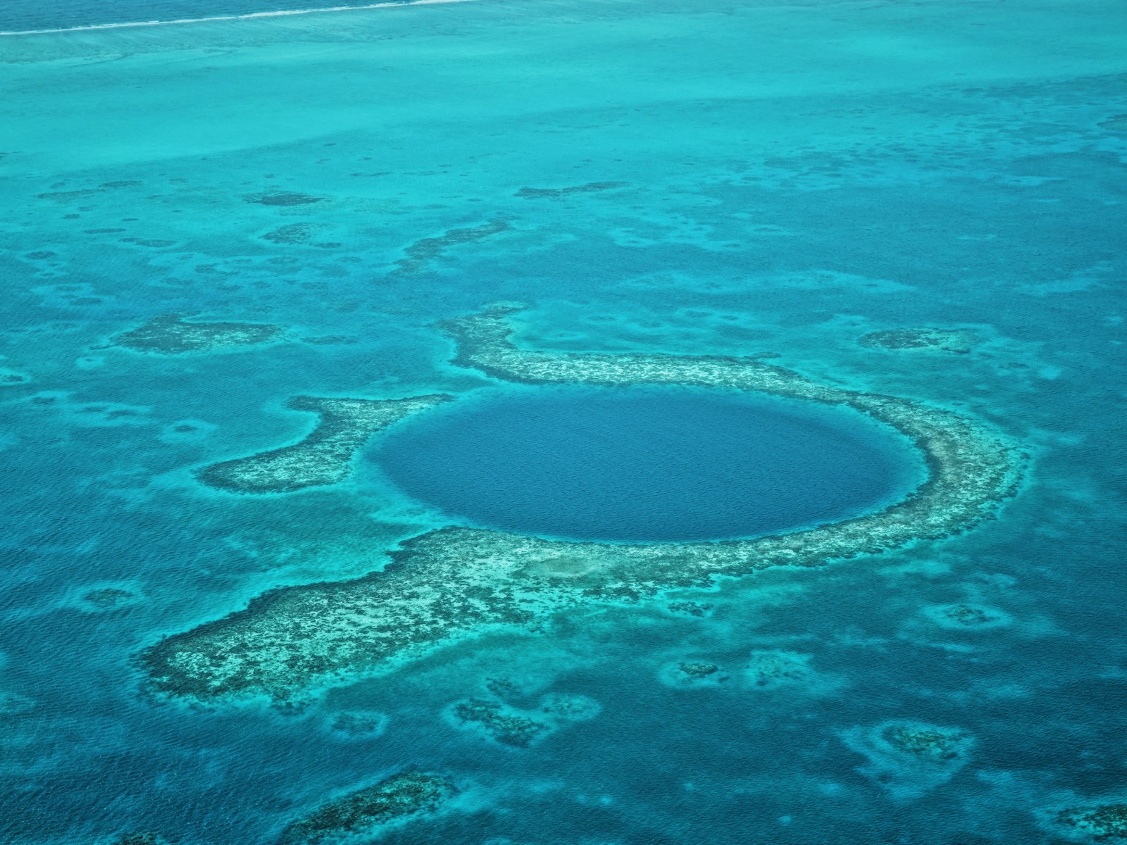 An aerial view of the Great Blue Hole ringed by turquoise reef off the coast of Belize