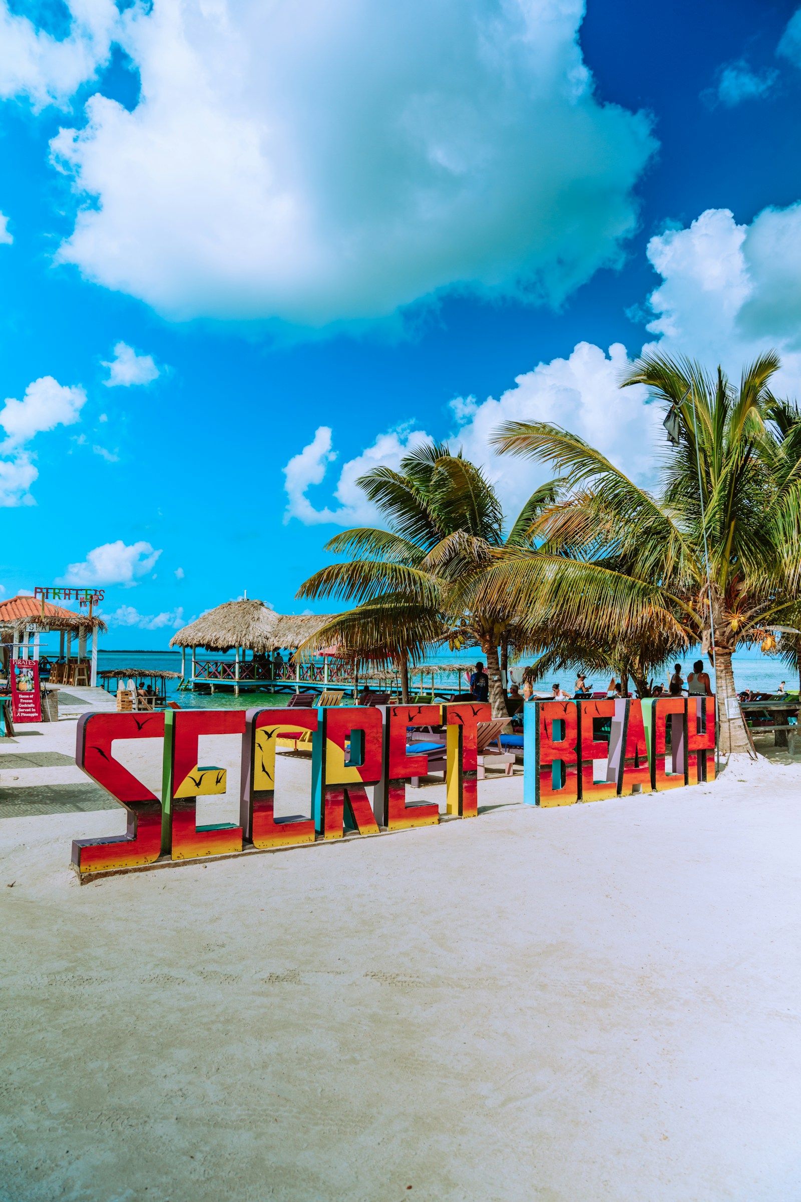 The colourful Secret Beach sign, palms, and turquoise water on Ambergris Caye, Belize