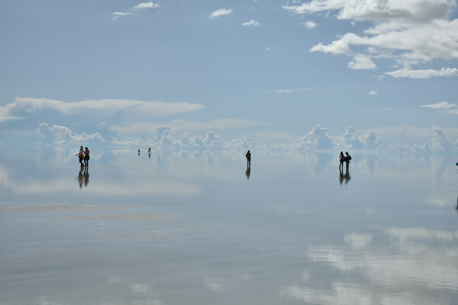 People appearing to walk on the sky as the flooded Salar de Uyuni mirrors the clouds in Bolivia