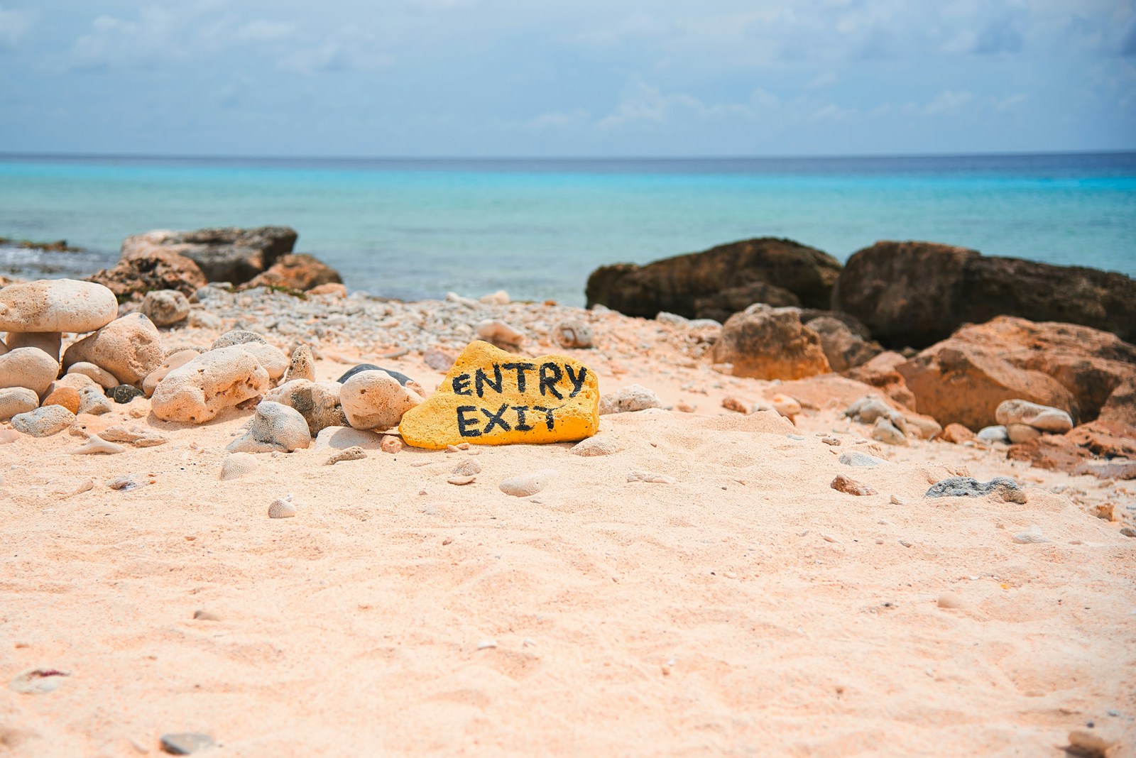 The yellow ENTRY EXIT shore-dive marker stone on a coral beach, Bonaire