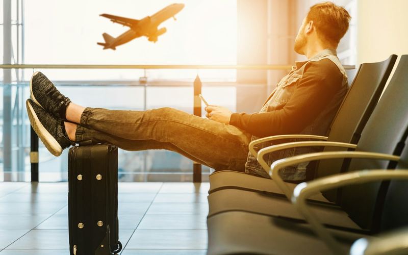 A traveler resting with a suitcase as a plane takes off