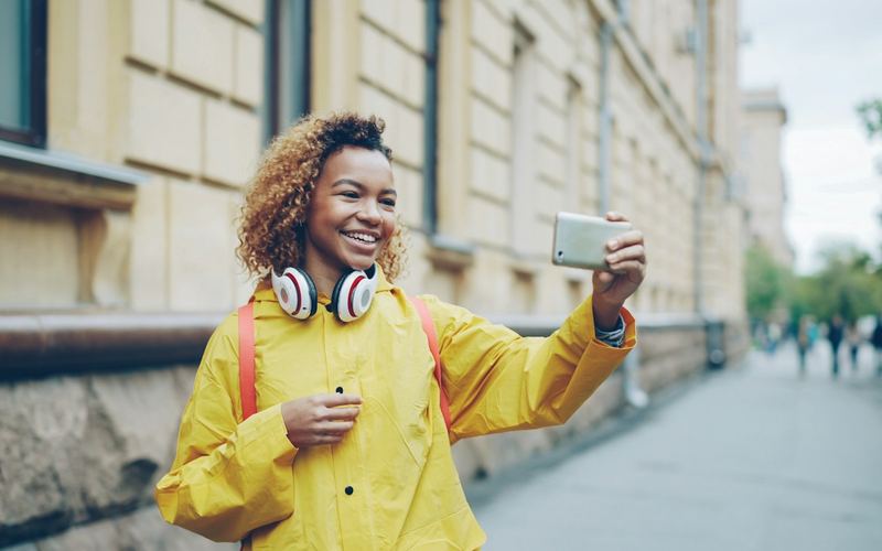 A smiling traveler in a yellow coat holding a phone