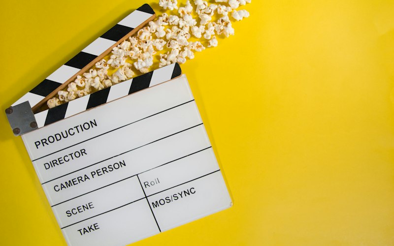 A movie clapperboard with popcorn on a yellow background