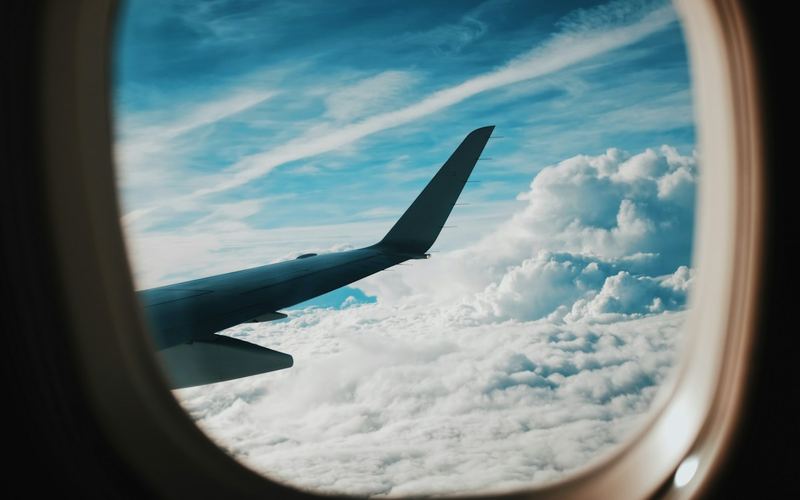 A plane wing seen through a window above the clouds