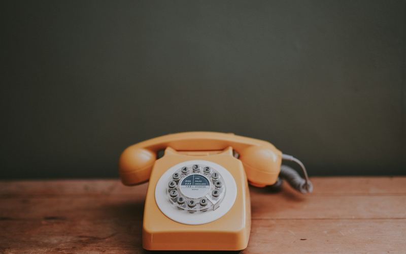 An orange rotary telephone on a wooden table