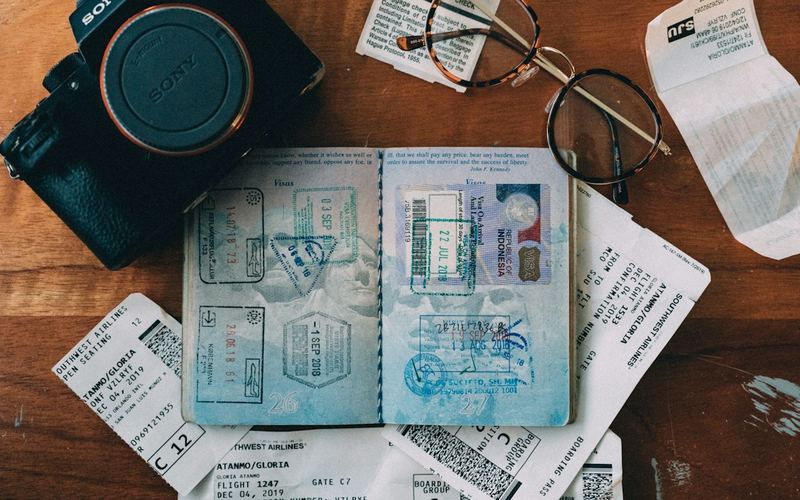 A stamped passport on a desk with a camera and tickets