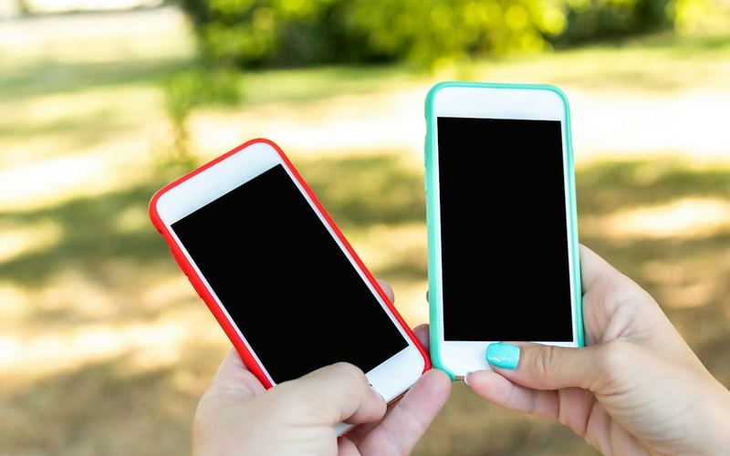 Two hands holding two phones in the sun