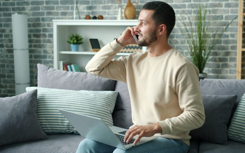 A man on a phone call on his sofa with a laptop on his lap