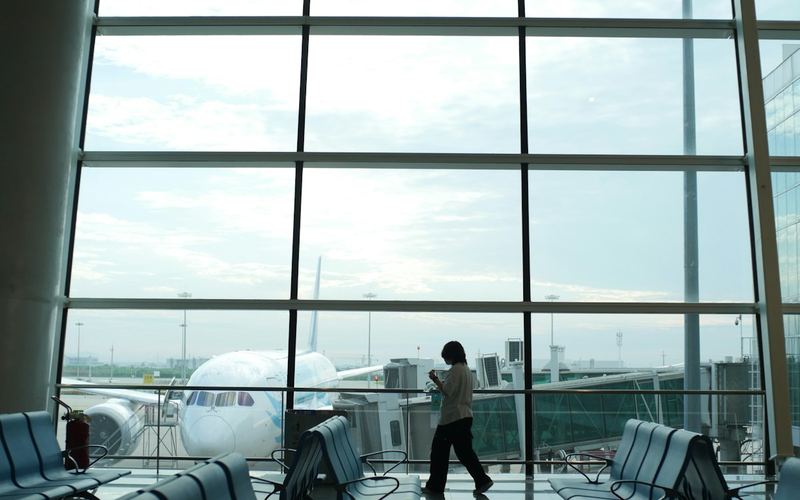 A traveler at an airport window watching a plane