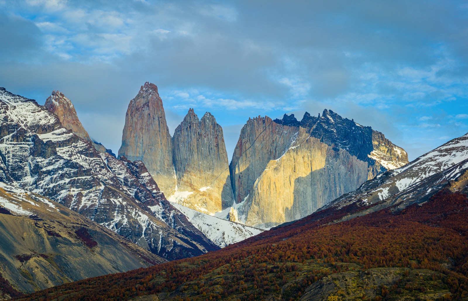 The granite towers of Torres del Paine rising above autumn forest in Patagonia