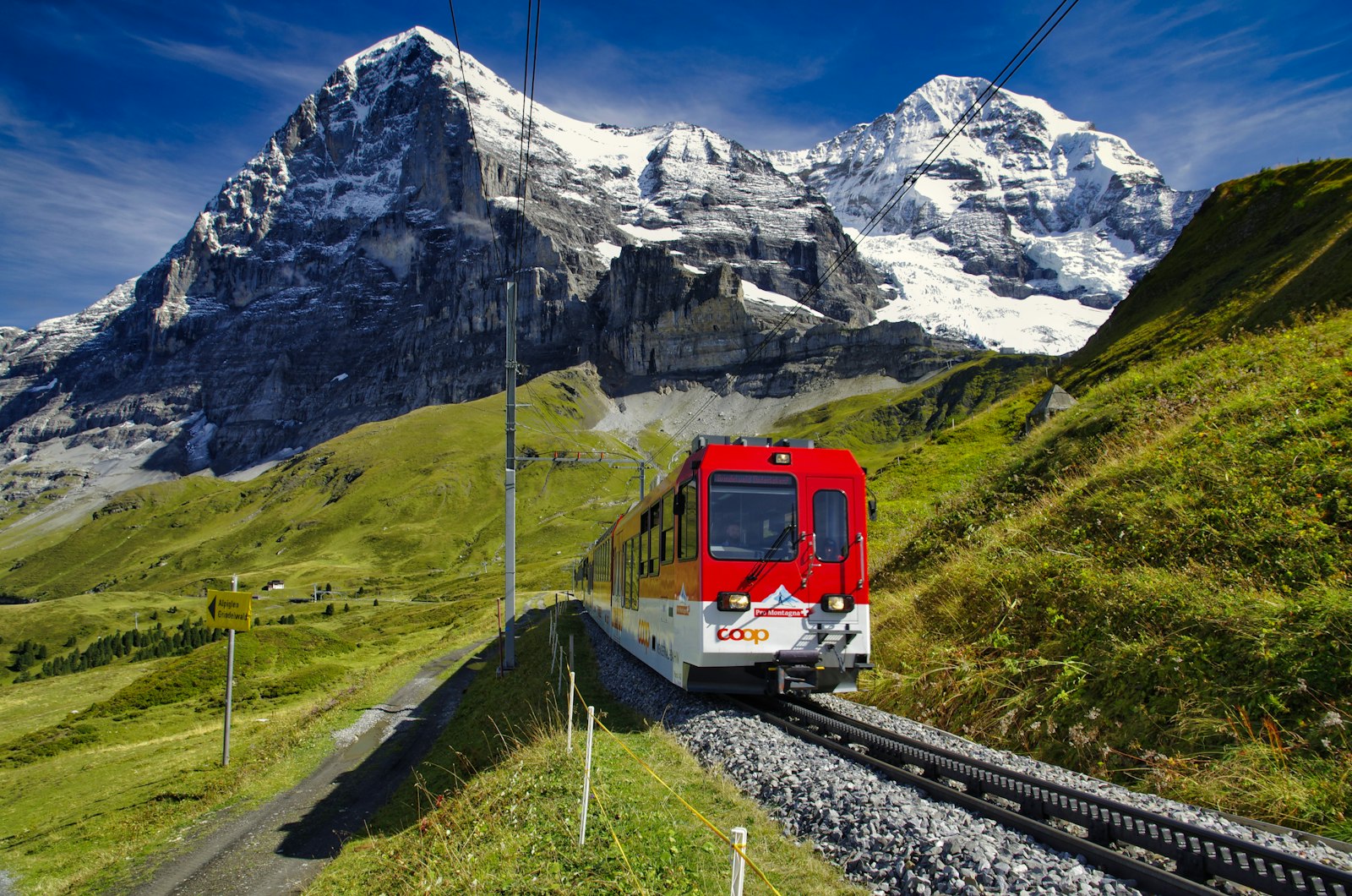 A red and white Swiss train on a mountain railway beneath snow-capped peaks