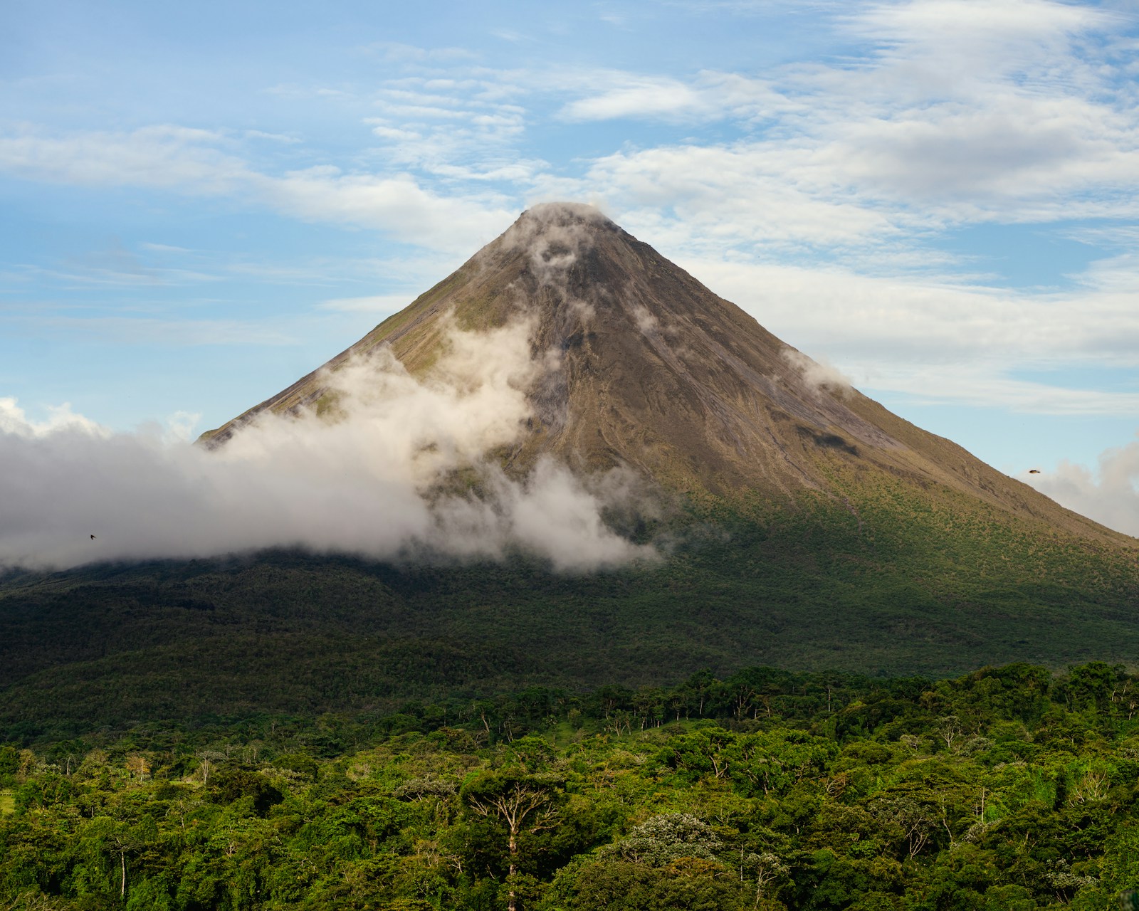 The conical Arenal volcano wreathed in cloud above dense rainforest in Costa Rica