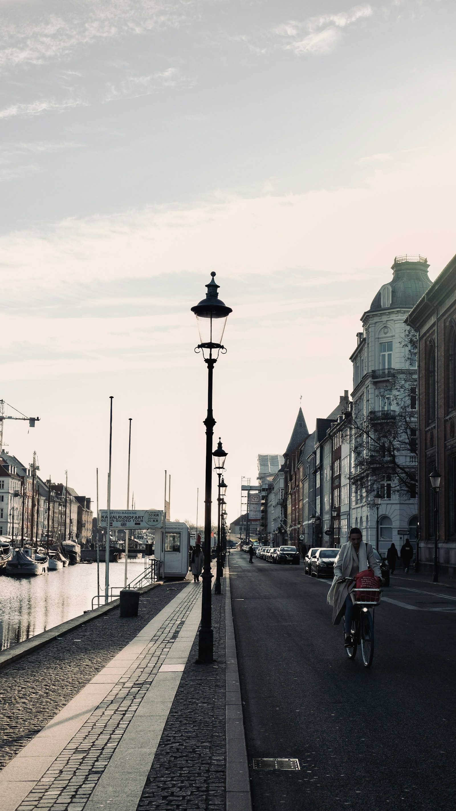 A cyclist riding along a Copenhagen canal lined with moored boats