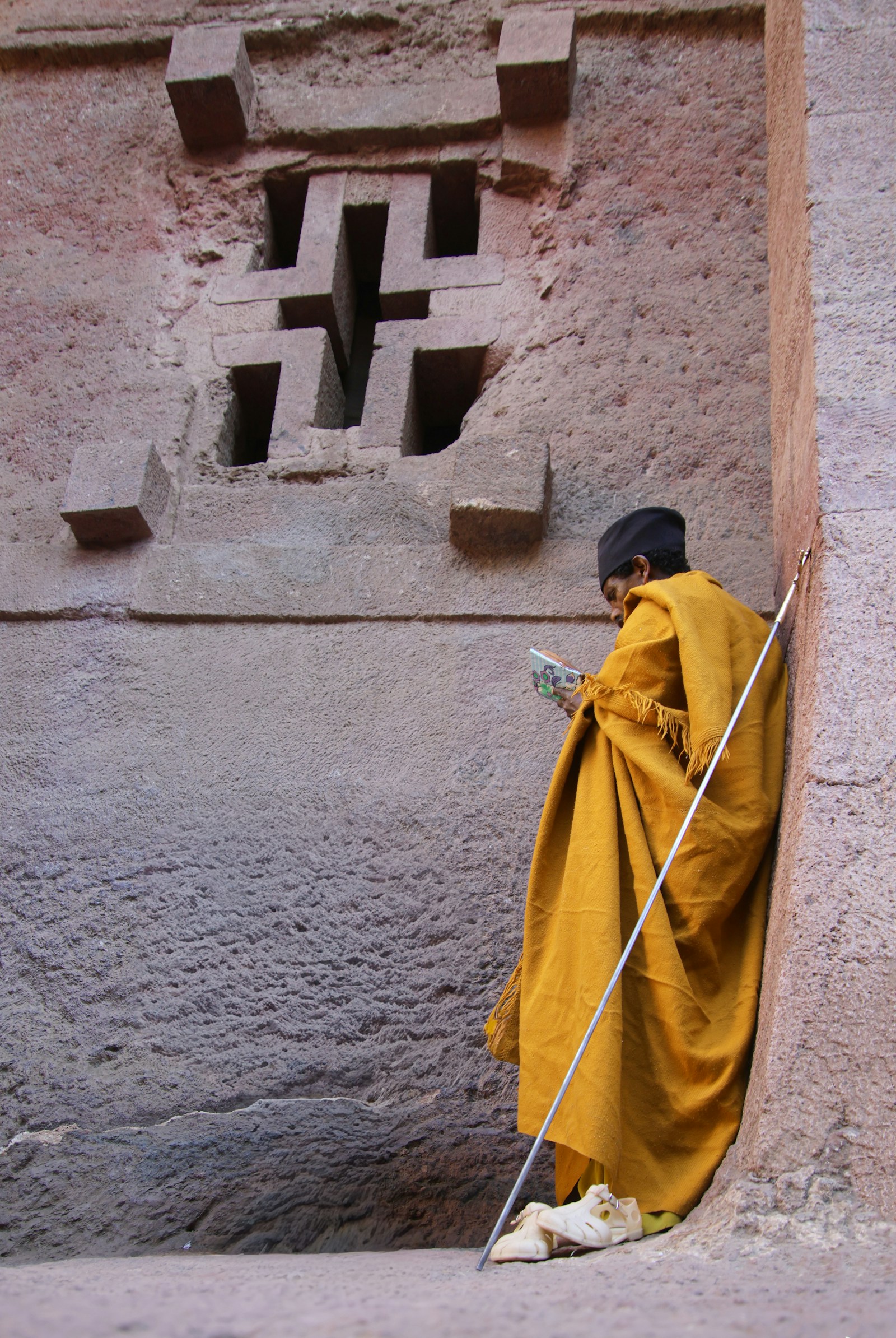 An Ethiopian Orthodox priest in a saffron robe reading beside a cross-shaped window at the rock-hewn churches of Lalibela