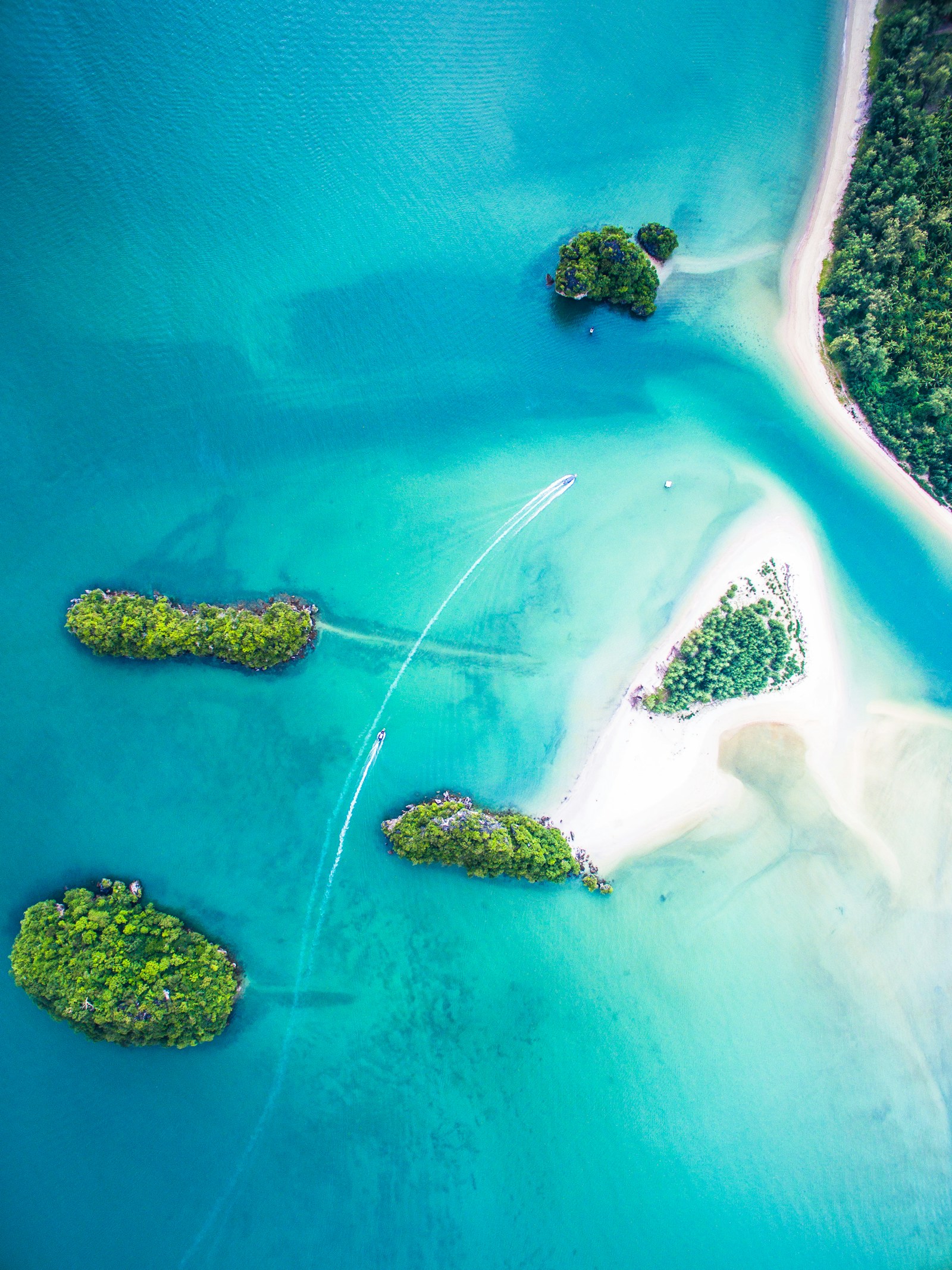 An aerial view of small green islets and turquoise lagoons with boats in Fiji