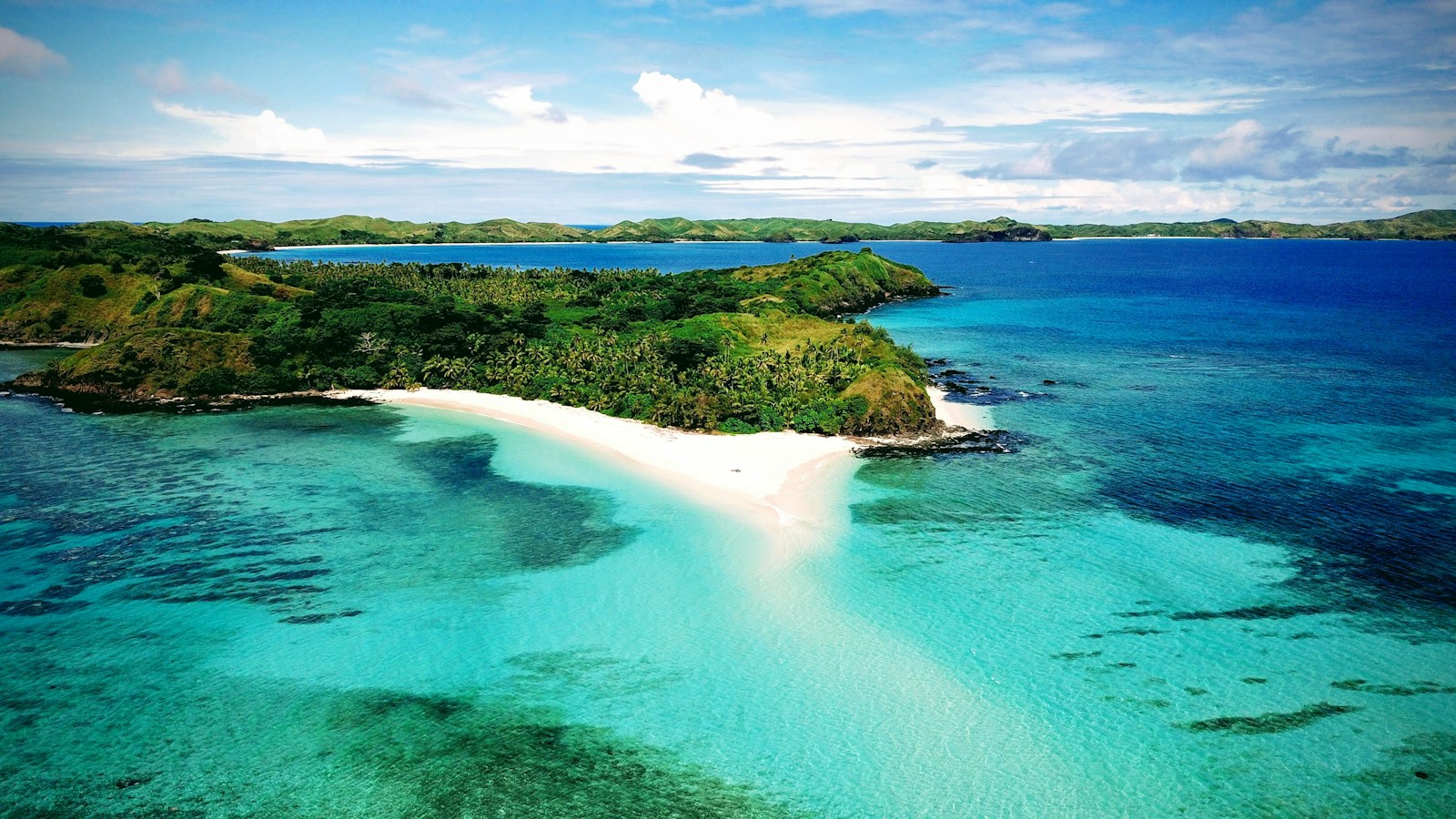 A green Fiji island with a white-sand beach and turquoise reef lagoon