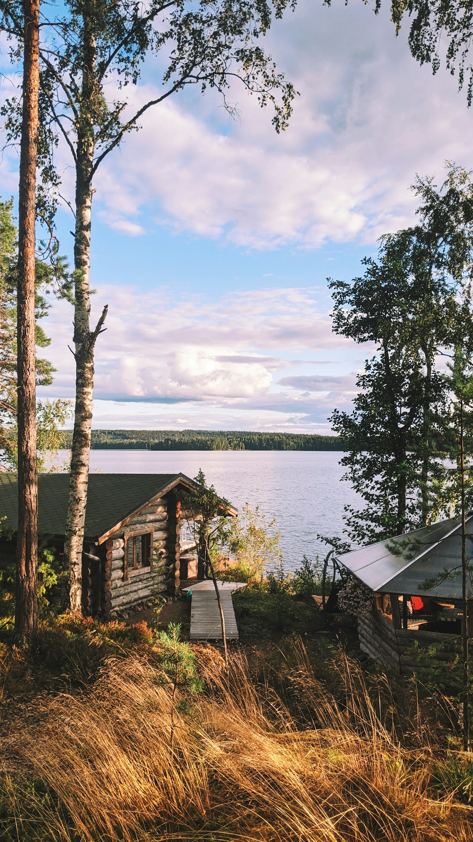 A traditional Finnish log cabin and jetty beside a calm forest lake at golden hour