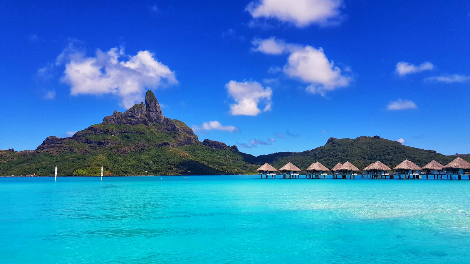 The jagged peak of Mount Otemanu over the turquoise lagoon and a row of overwater bungalows, Bora Bora