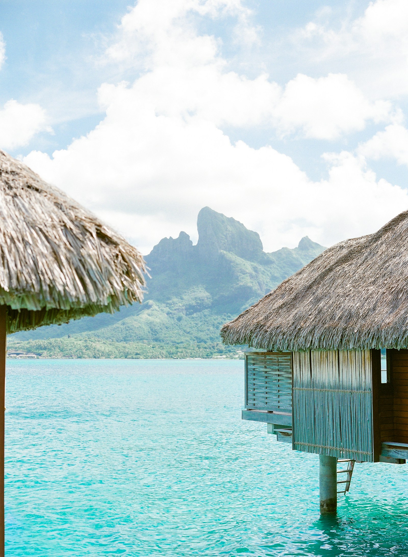 A thatched overwater bungalow with Mount Otemanu across the turquoise lagoon, Bora Bora