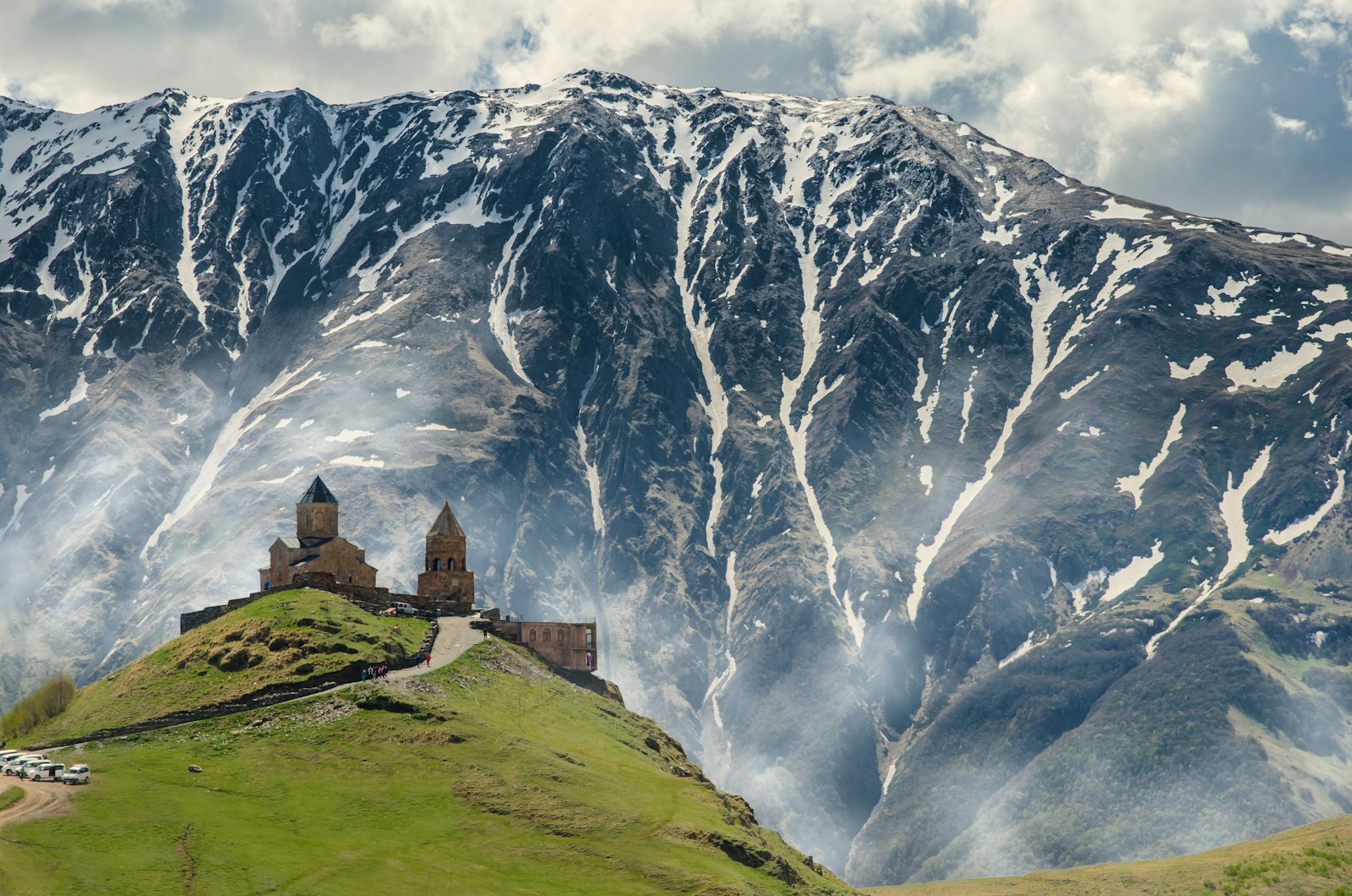 The Gergeti Trinity Church on a green hill below the snow-streaked Caucasus at Kazbegi