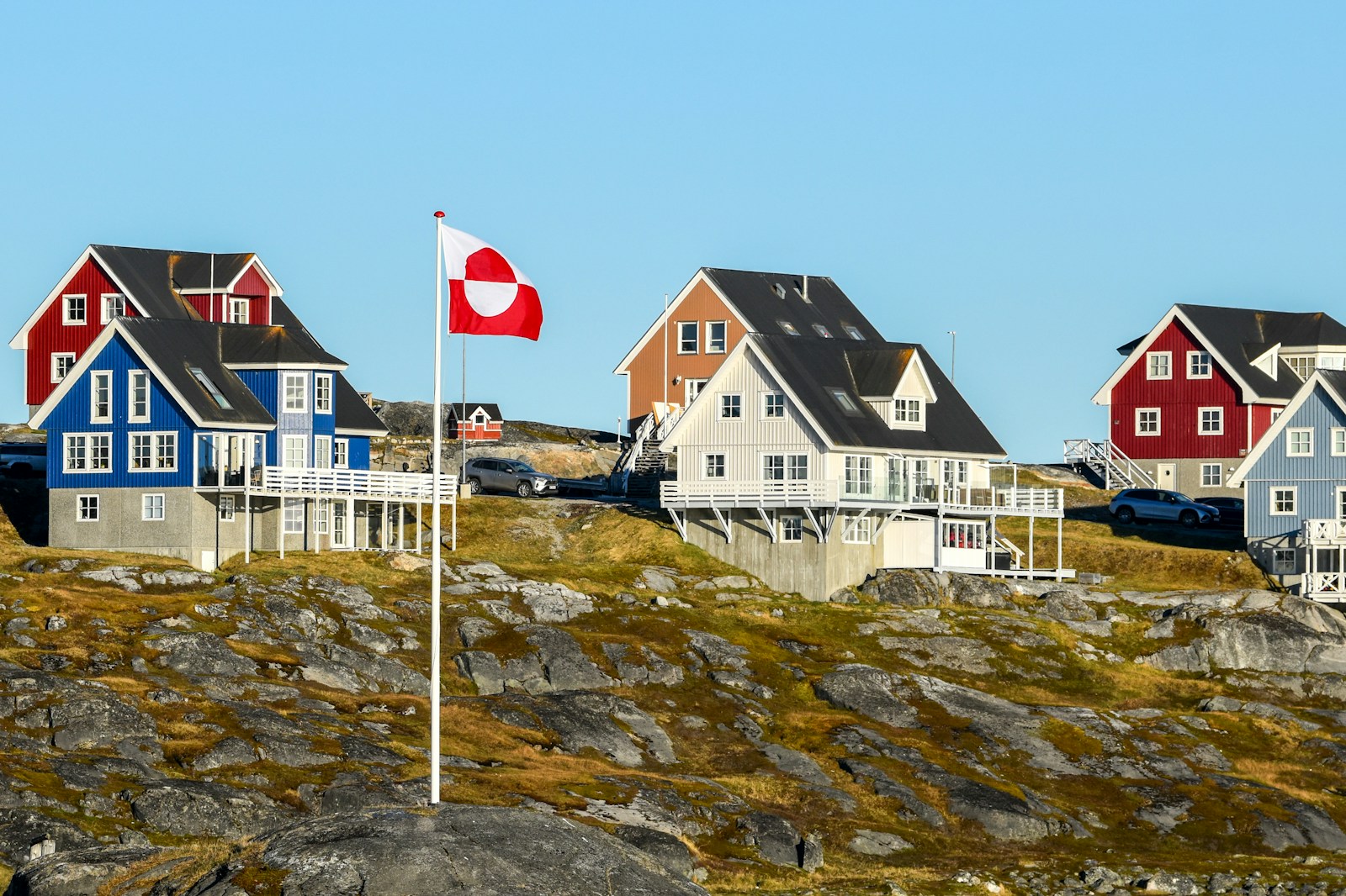Colourful wooden houses on a rocky hill with the Greenland flag flying, Nuuk