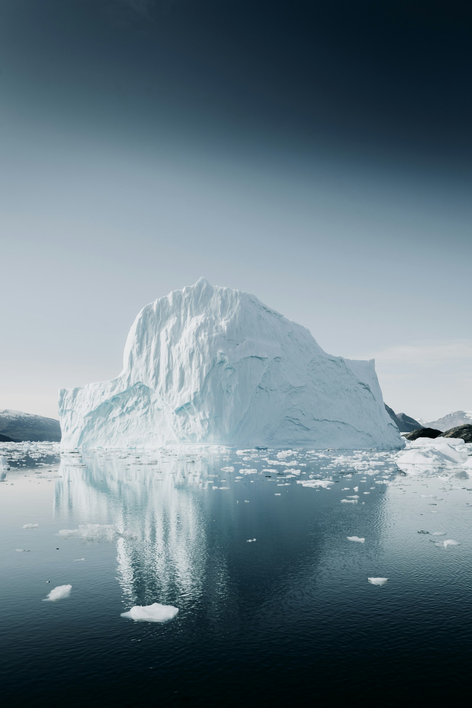 A giant iceberg floating in calm arctic water with brash ice and distant mountains, Greenland
