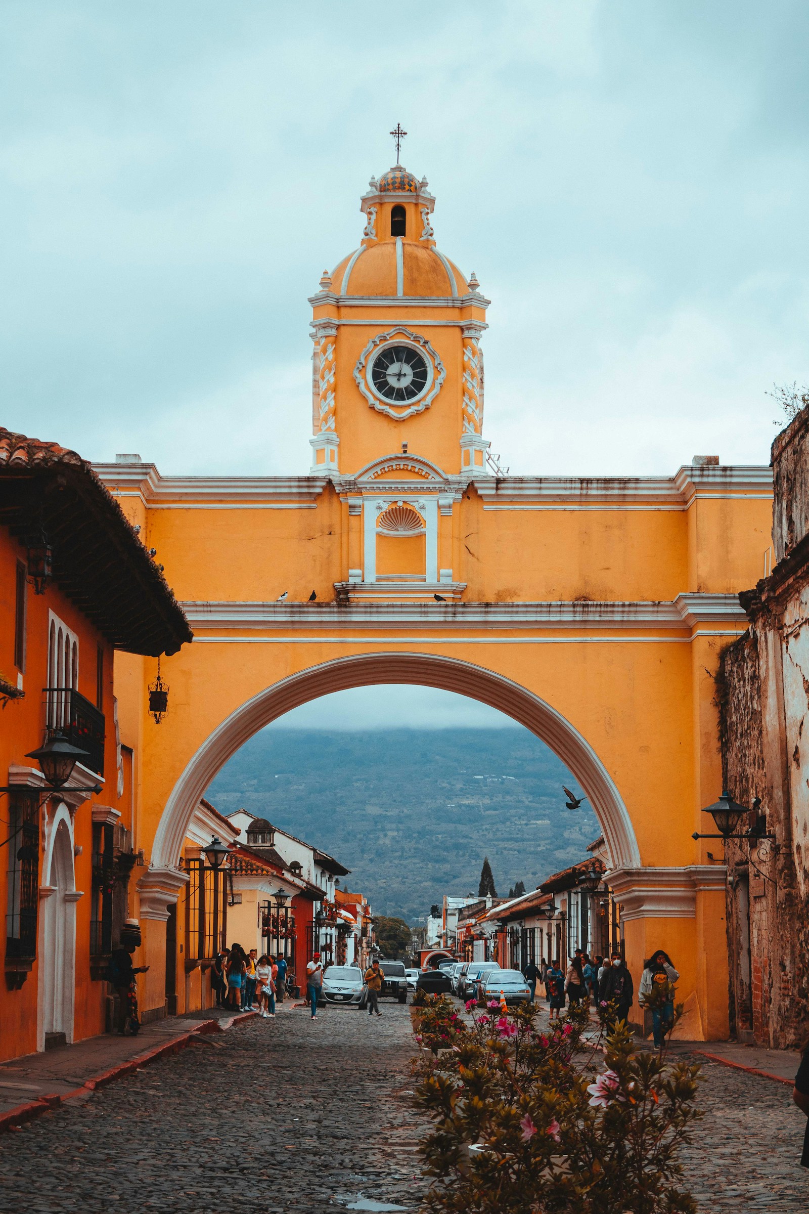 The yellow Santa Catalina Arch and clock tower framing a volcano on a cobblestone street in Antigua, Guatemala