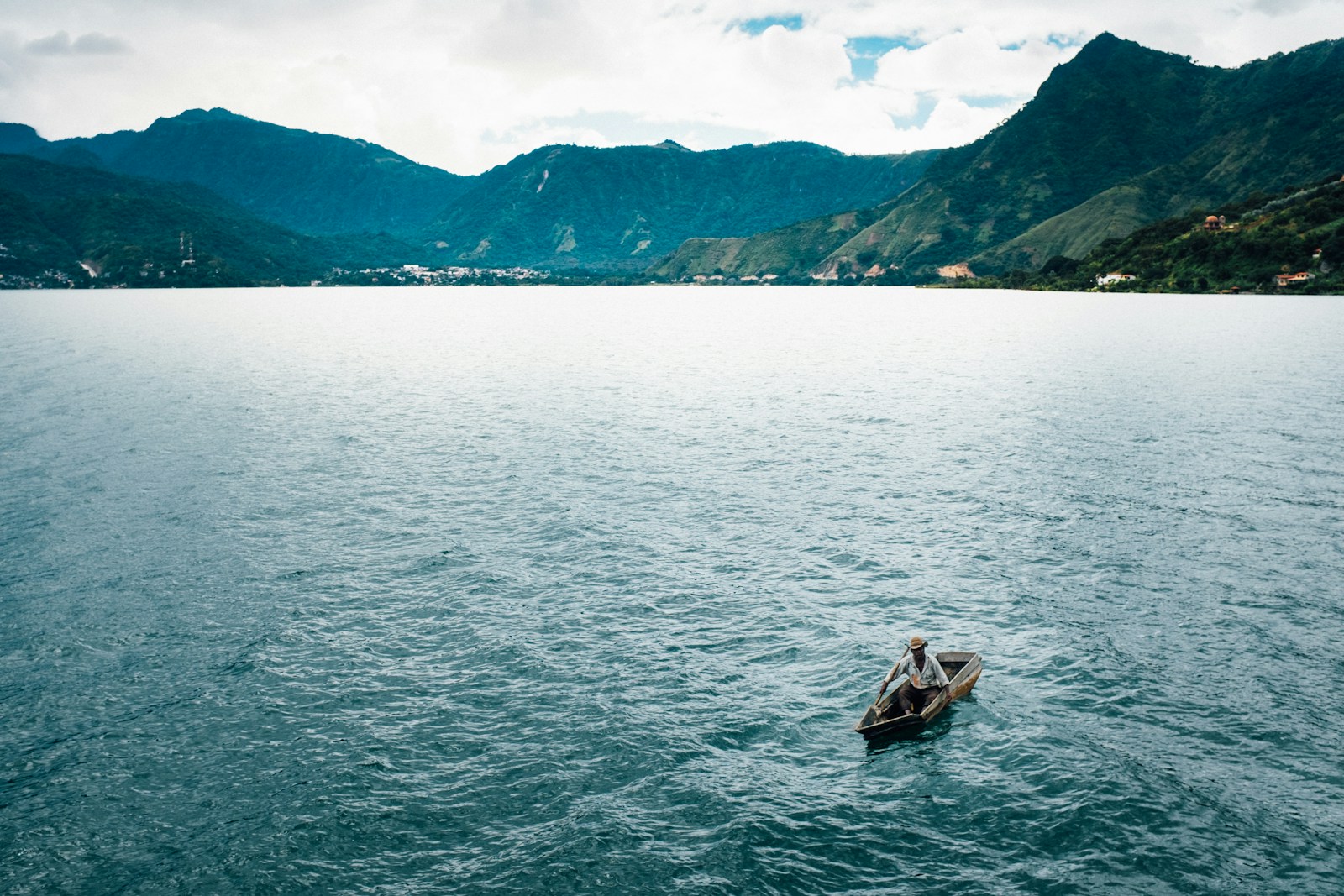 A lone fisherman in a wooden boat on volcano-ringed Lake Atitlan in Guatemala