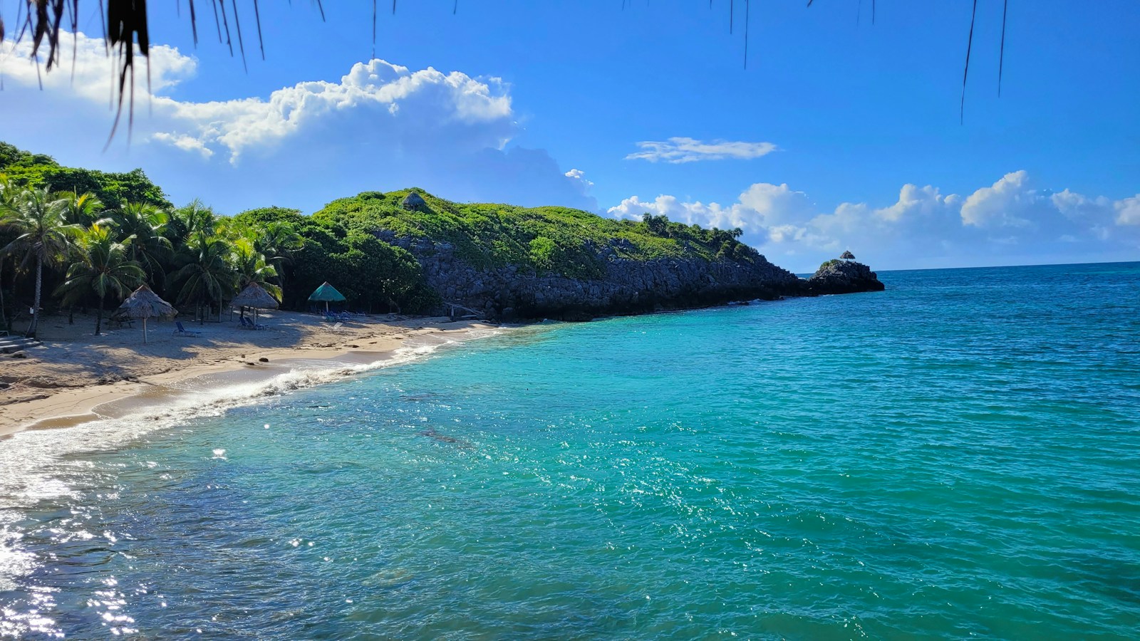 A palm-fringed turquoise cove with thatched umbrellas on Roatan in the Bay Islands, Honduras