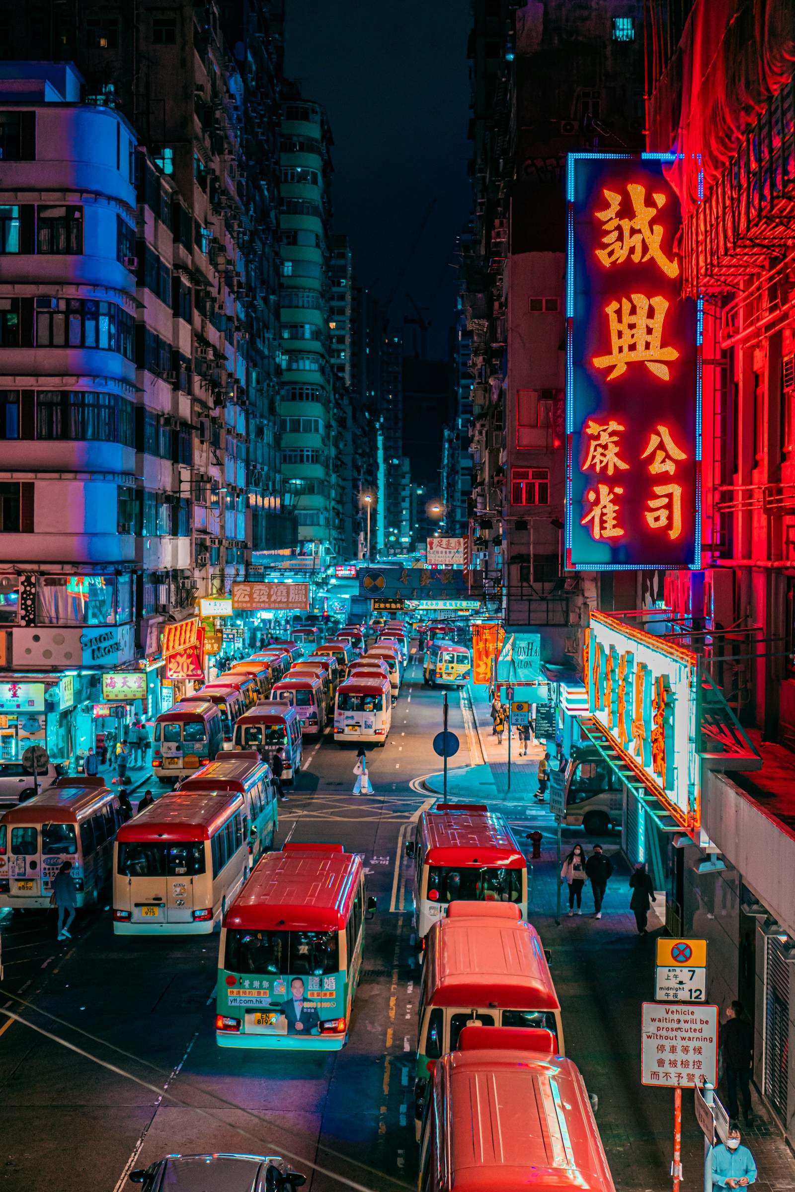 Red minibuses lined up beneath glowing neon signs on a Mong Kok street at night, Hong Kong