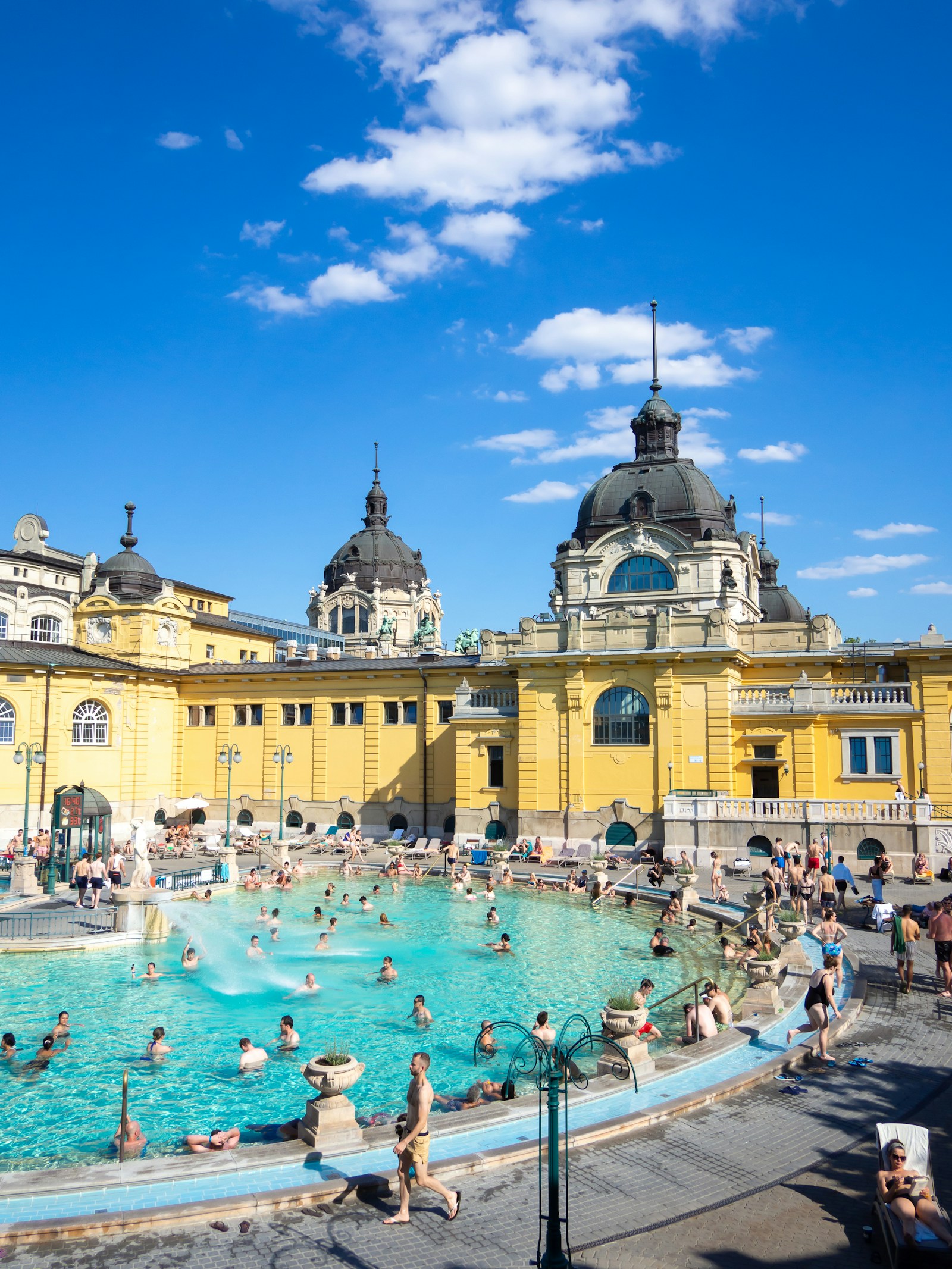 Bathers in the turquoise outdoor thermal pool below the yellow neo-baroque Szechenyi baths in Budapest