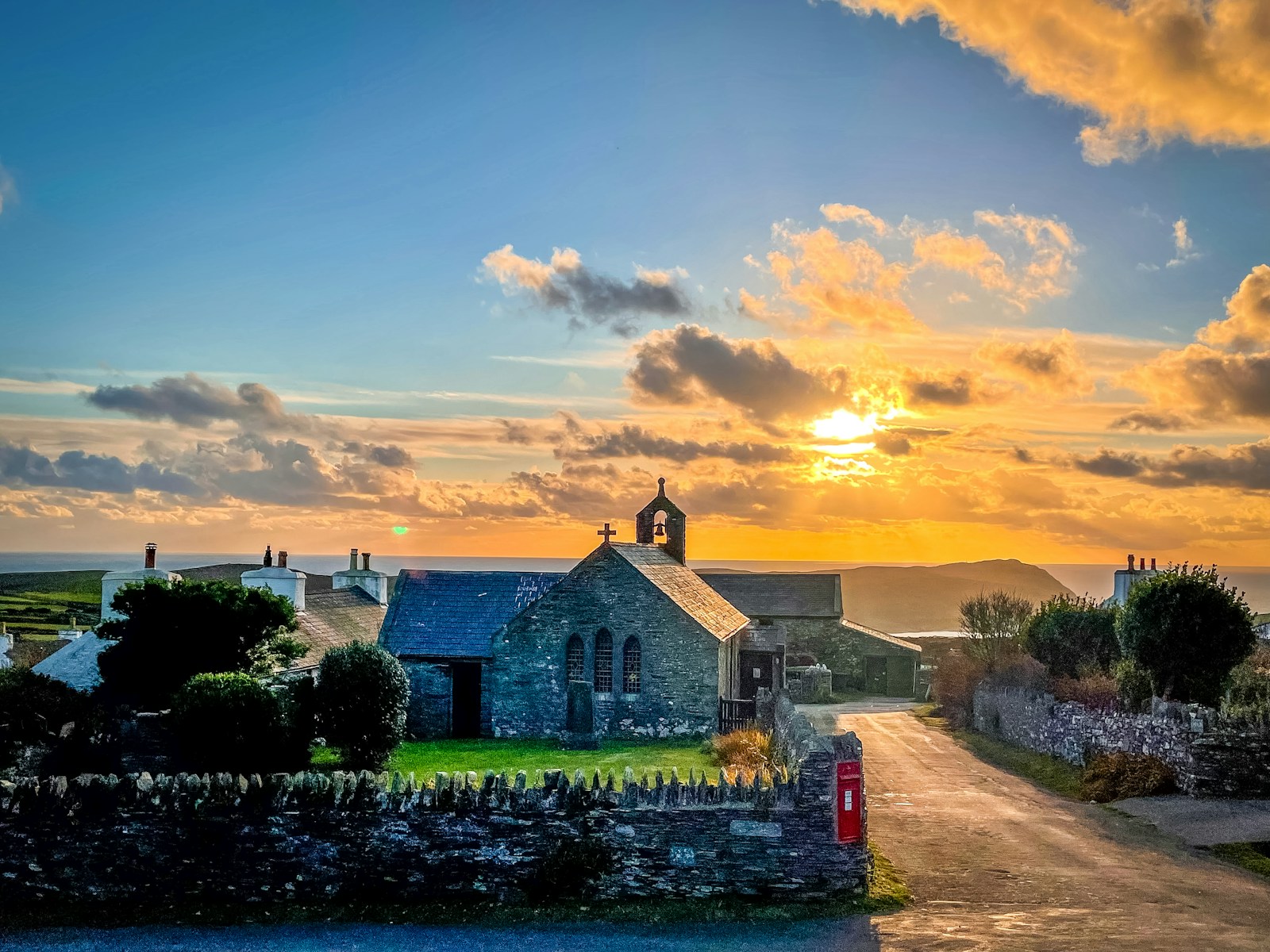 A stone church with a red postbox and drystone walls at sunset, Isle of Man