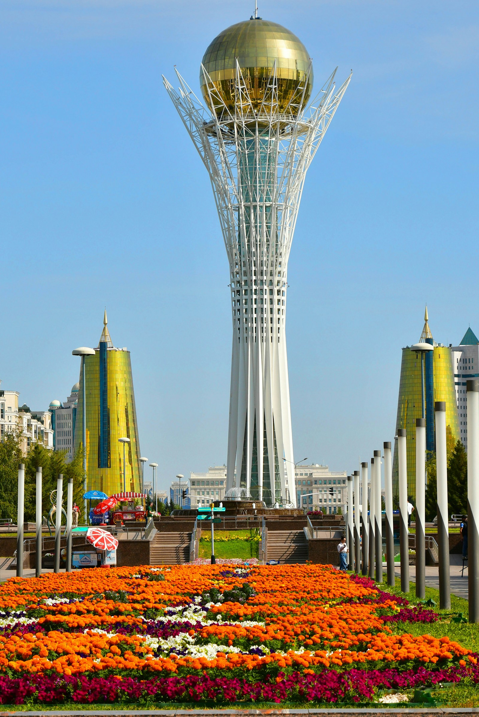 The golden-orbed Bayterek Tower framed by twin golden towers and marigold beds in Astana, Kazakhstan