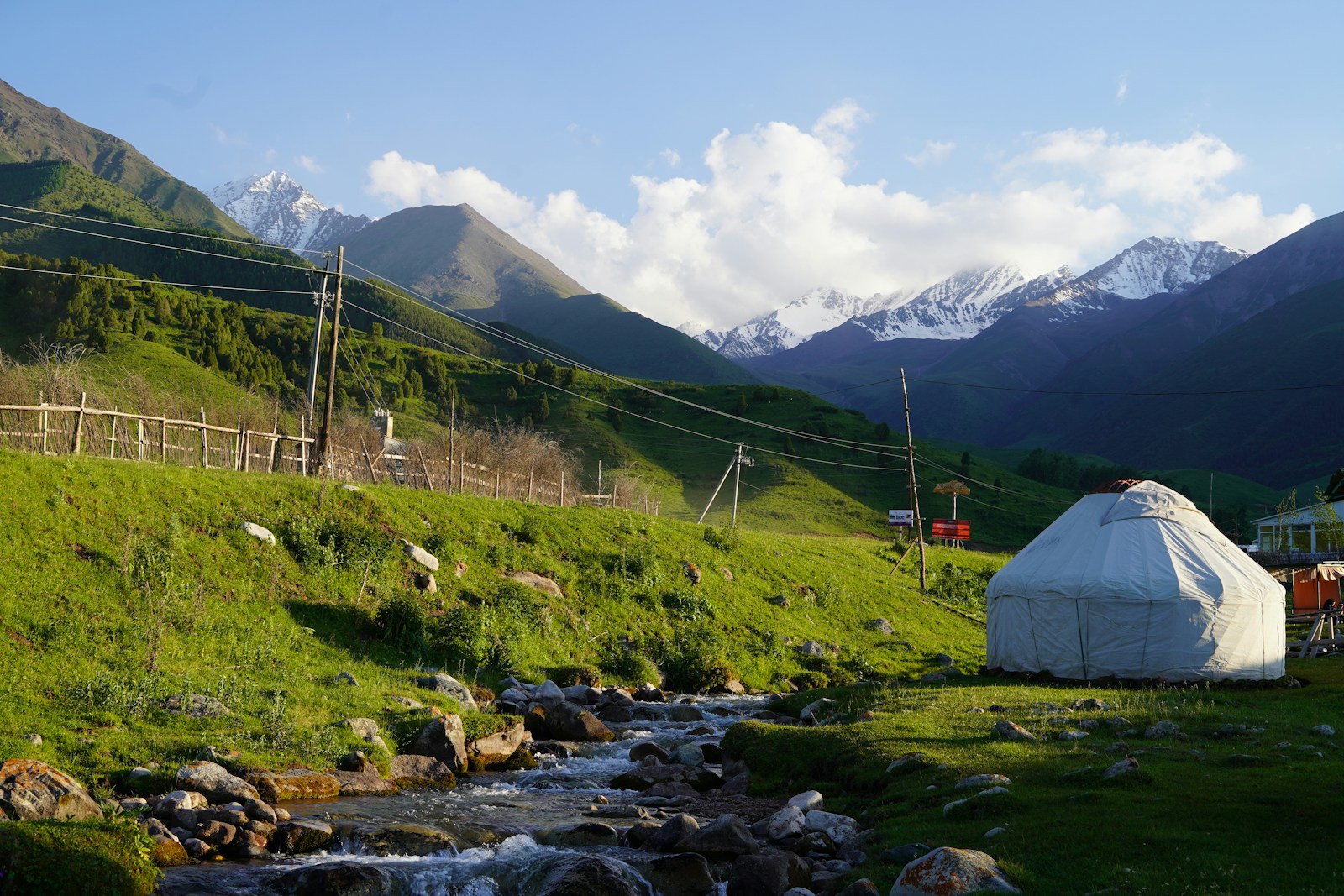 A white yurt beside a mountain stream below the snow-capped Tian Shan in Kyrgyzstan