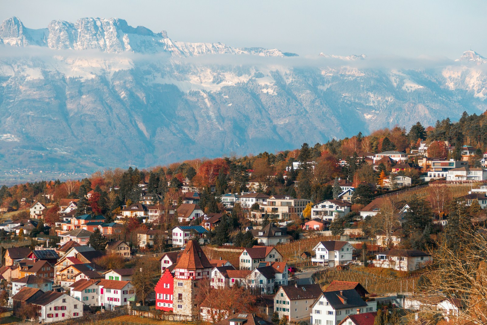 A Liechtenstein town with the Red House below snow-capped Alps across the Rhine valley