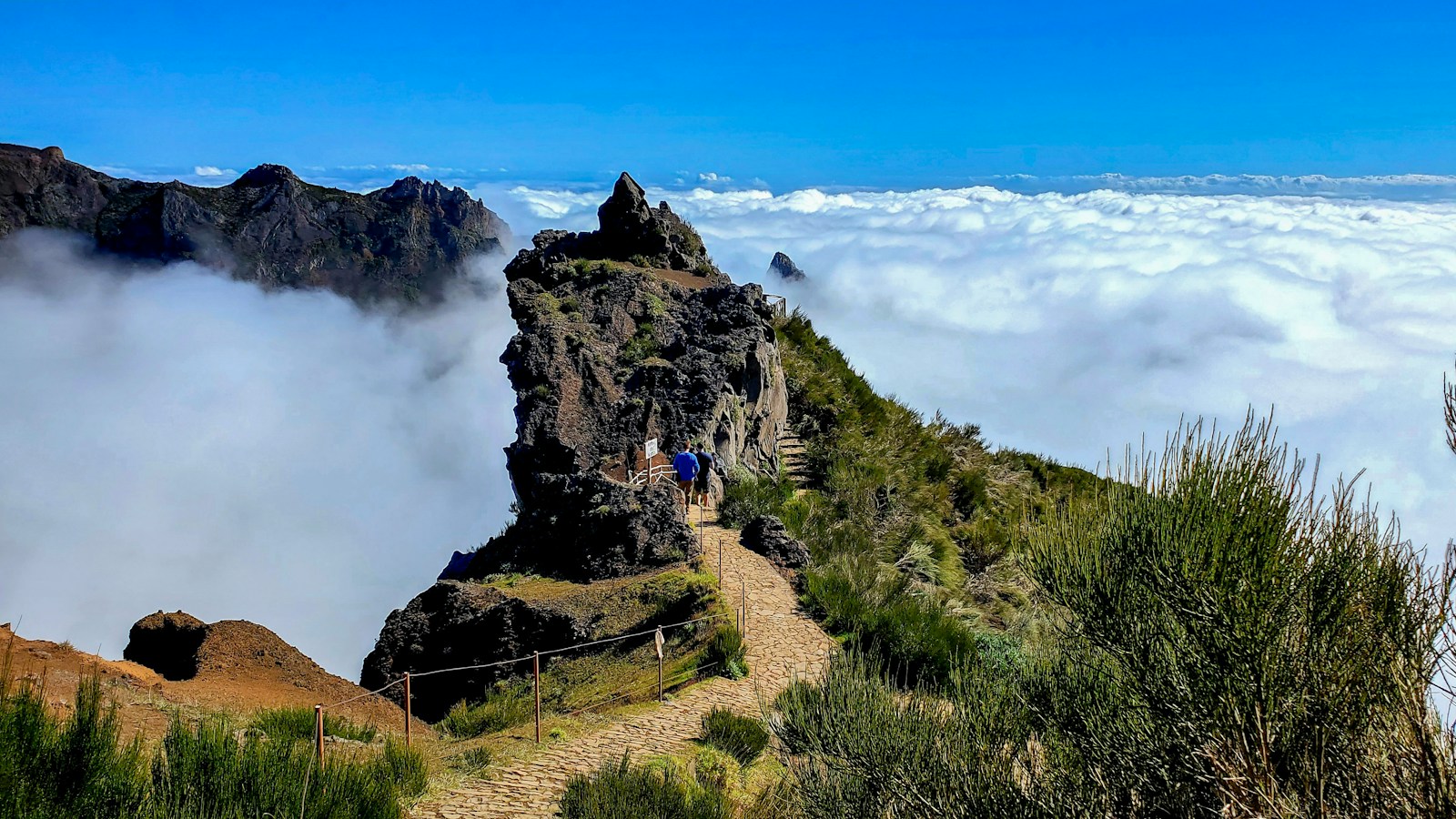 A hiker on the Pico do Areeiro ridge trail above a sea of clouds, Madeira