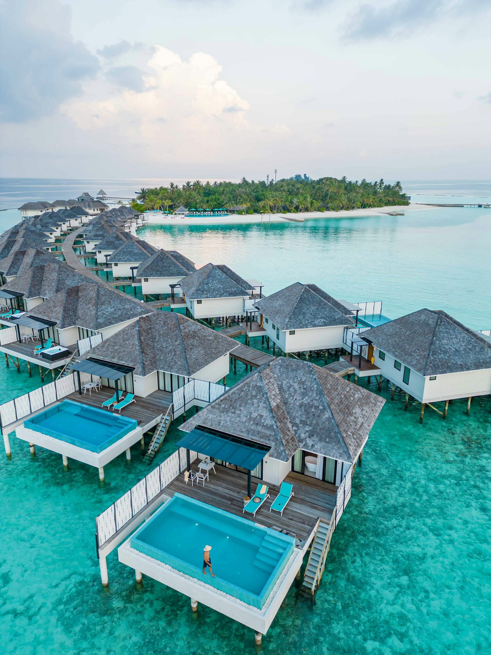 An aerial view of overwater villas with plunge pools curving along a turquoise Maldives lagoon