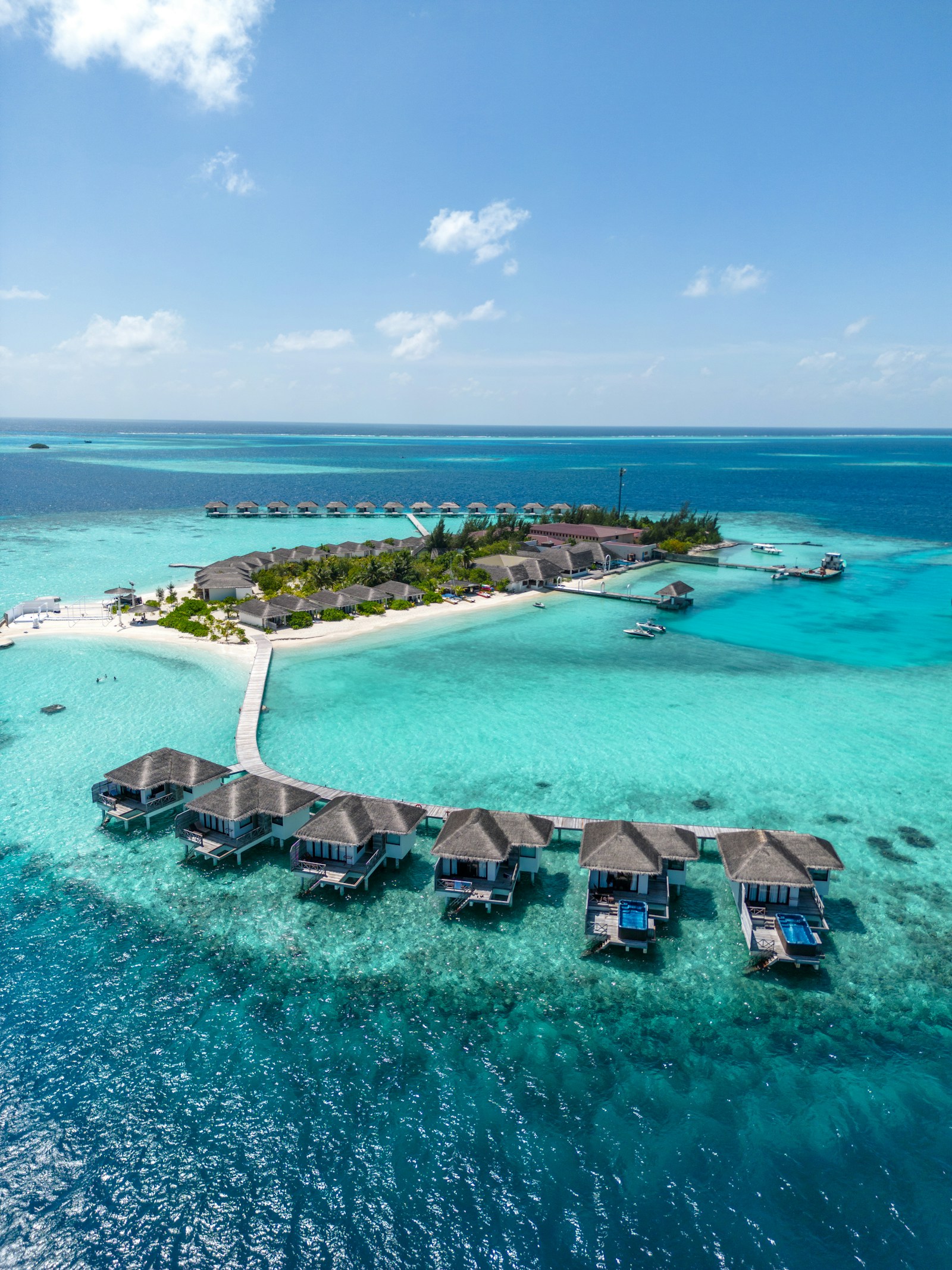 An aerial view of a Maldives resort island with overwater bungalows and white-sand beaches