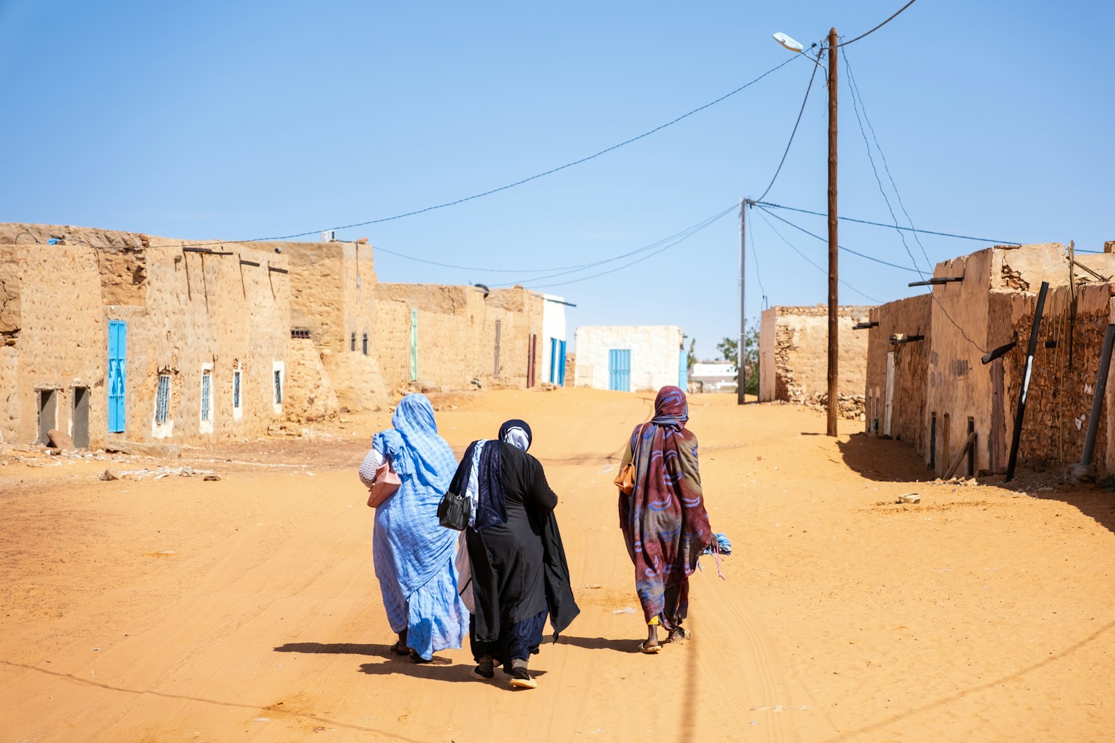 Women in melhafas walking a sandy street of adobe houses in Chinguetti, Mauritania