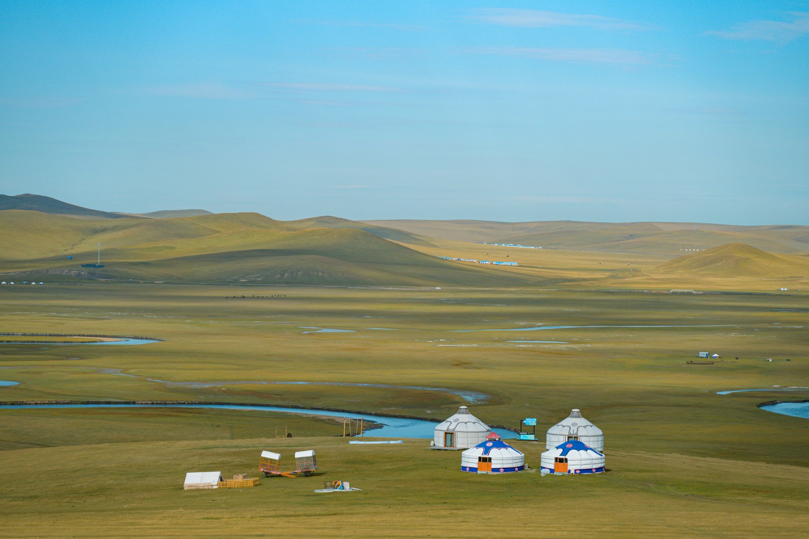 White felt gers on the vast green Mongolian steppe beside a winding river