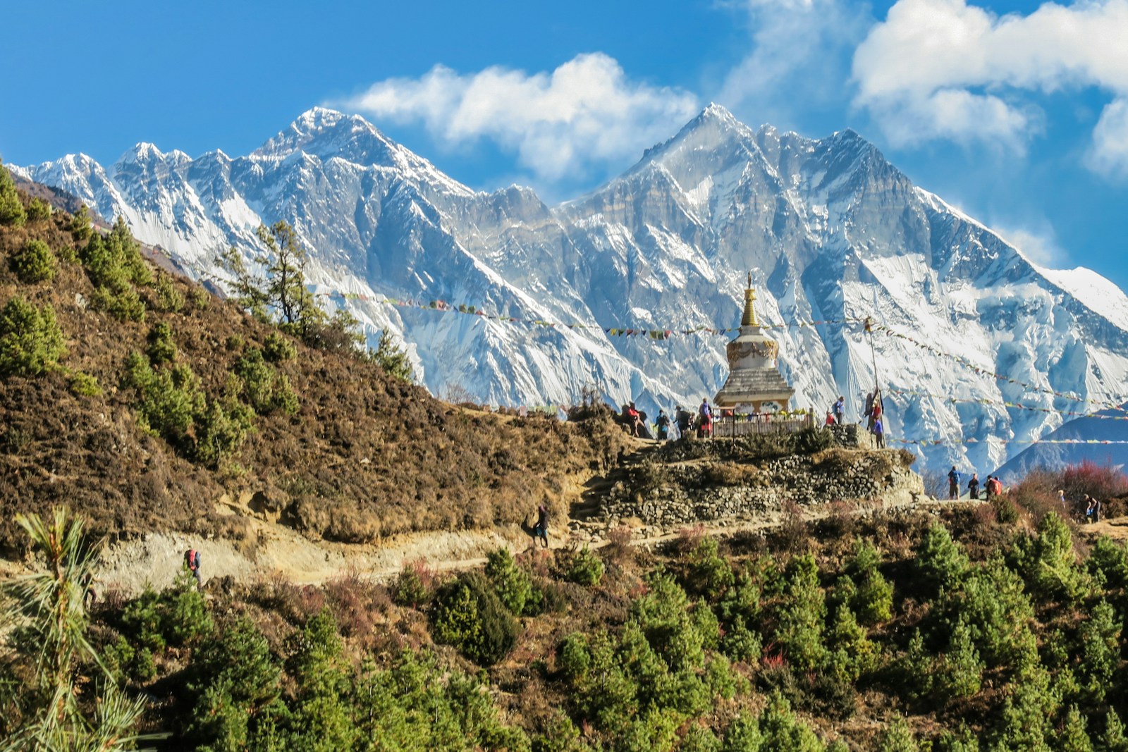 A stupa and prayer flags on the Everest trail below the snow peaks, with trekkers passing