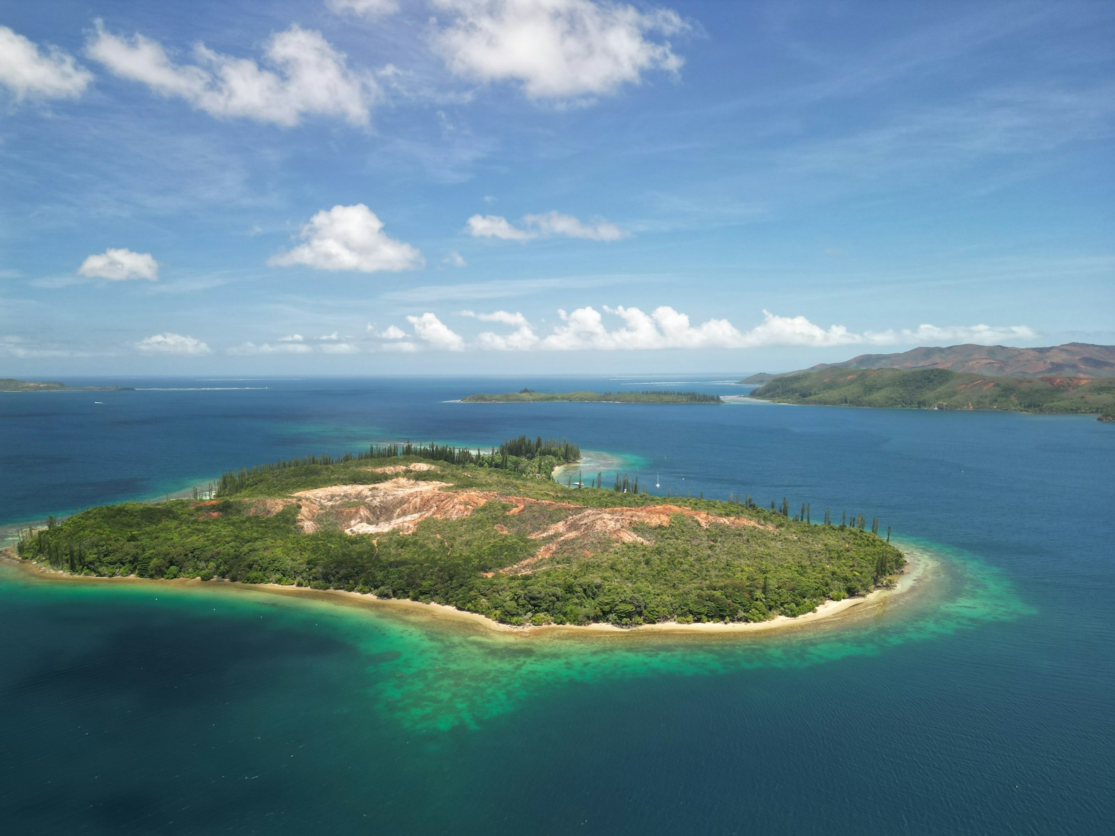 An aerial view of a reef island with Cook pines and red earth in the lagoon, New Caledonia
