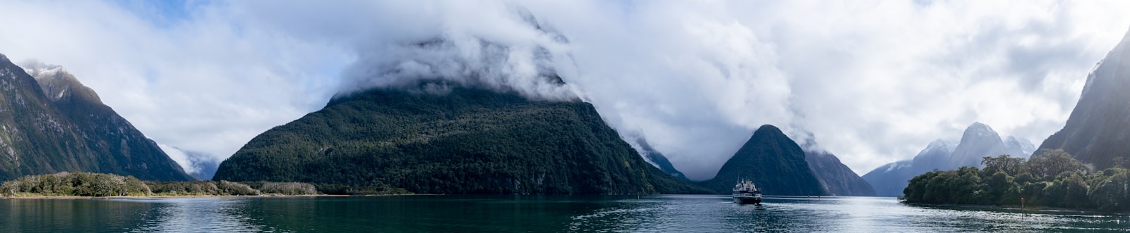 Cloud-wreathed peaks and a cruise boat on Milford Sound in Fiordland