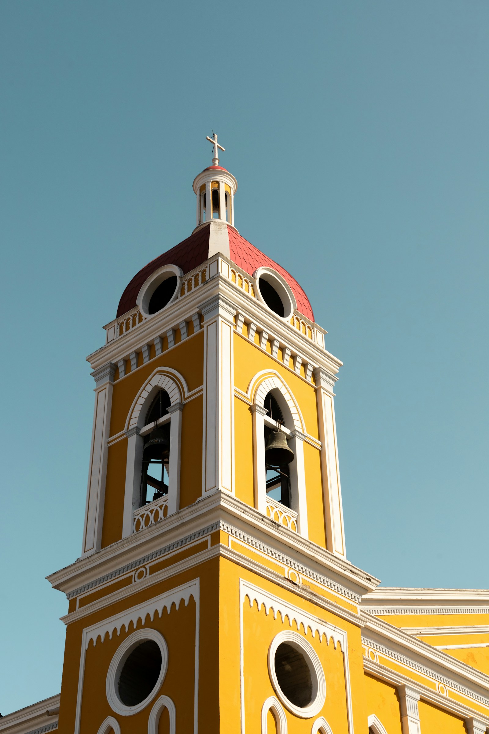 The bright yellow bell tower and red dome of the cathedral of Granada against a clear sky, Nicaragua