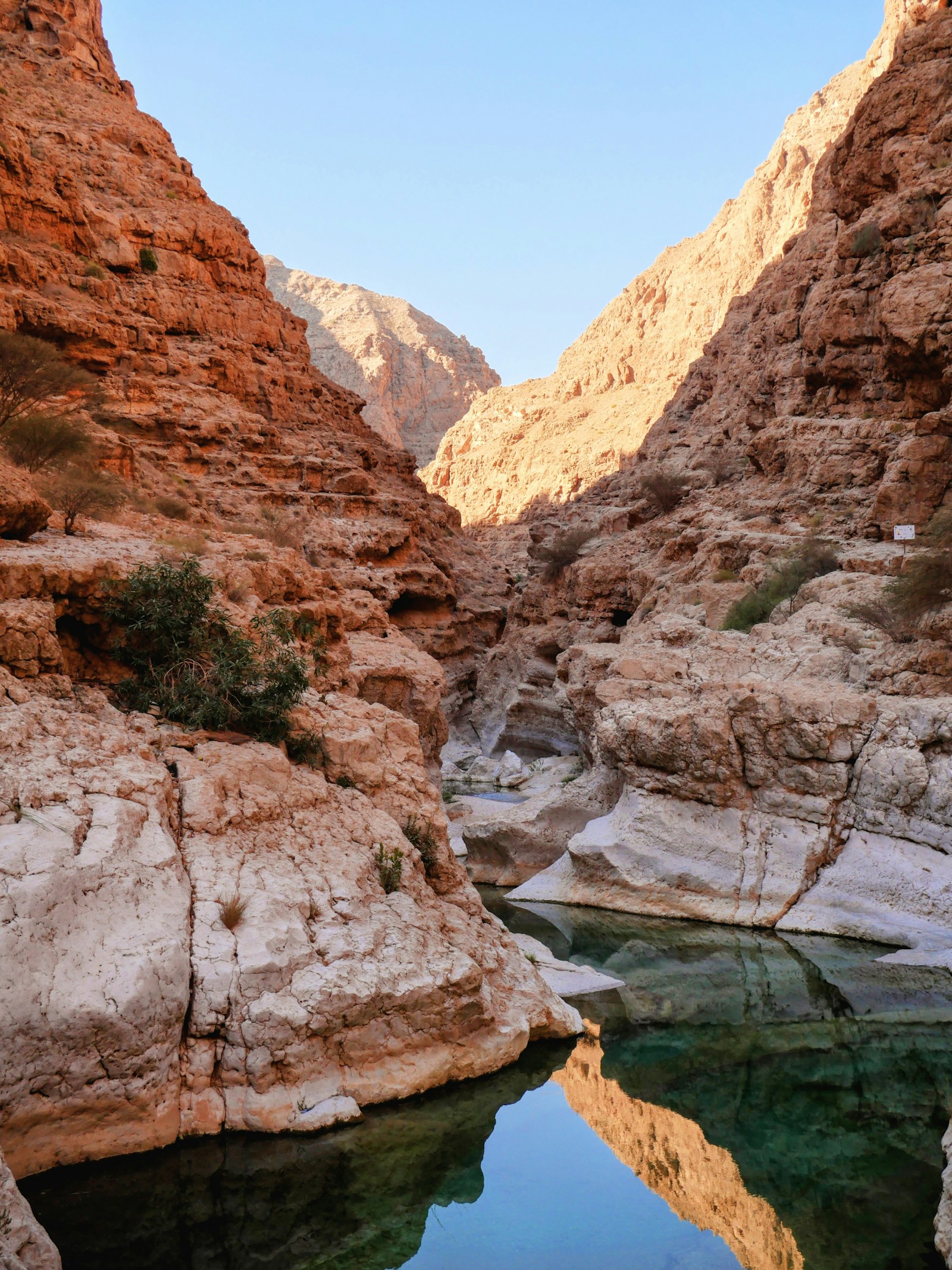 A turquoise pool between towering rock cliffs in a wadi canyon in Oman